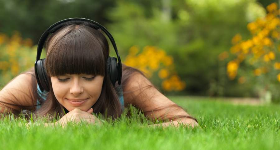 Girl listening to music on headphones laying in the grass.